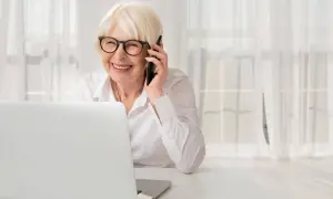 Uśmiechnięta starsza pani w okularach rozmawia przez telefon, siedząc przy laptopie. Dyskutuje o służebności mieszkania i obowiązkach właściciela.