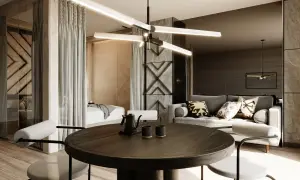 Nowoczesny apartament inwestycyjny z częścią sypialnianą oddzieloną zasłonami, salonem z szarą sofą i okrągłym stołem jadalnianym.