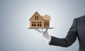 Dłoń w białej rękawiczce podaje model domu na tacy. Czy to oferta z maksymalną prowizją pośrednika nieruchomości?