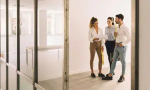 Trzy osoby omawiają dokumenty w pustym lokalu użytkowym. Może to być kontrola przed nałożeniem kary za mieszkanie w lokalu użytkowym.
