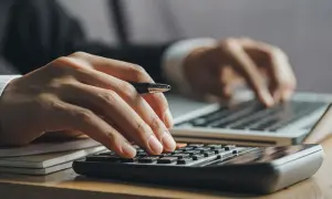 Ręce liczą na kalkulatorze i piszą na laptopie. Kluczowe pytanie: ile trzeba zarabiać żeby dostać kredyt na mieszkanie?