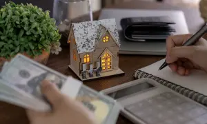Planujesz zakup domu? Sprawdź, ile trzeba zarabiać, żeby dostać 300 tys. kredytu. Na stole pieniądze, kalkulator i model domu.