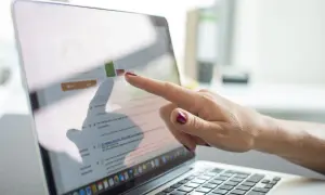 Dłoń wskazuje na ekran laptopa z wykresem i tekstem, prezentując prospekt informacyjny dotyczący optymalizacji SEO.