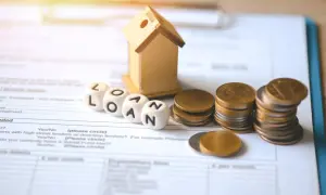 Domki, kostki z napisem LOAN, monety i dokumenty. Dylemat: lepiej zmniejszyć ratę czy skrócić okres kredytowania?