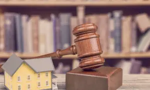 Młotek sędziowski i model domu na tle regałów z książkami. Symbolizuje licytację nieruchomości za mały dług.