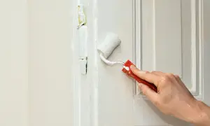 Ręka maluje białą farbą drzwi wałkiem. Zastanawiasz się, za ile sprzedać mieszkanie do remontu?