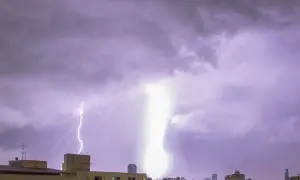 Potężne uderzenie pioruna w dom podczas burzy. Niebo rozświetlone błyskawicami nad miastem.