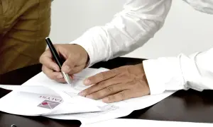Podpisanie aktu własności domu. Dwie osoby przy stole, jedna podpisuje dokumenty.