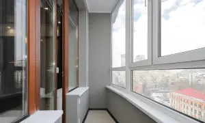 Wnętrze balkonu typu loggia z drewnianymi drzwiami i dużymi oknami, z widokiem na miasto.