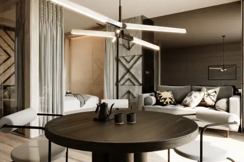 Nowoczesny apartament inwestycyjny z częścią sypialnianą oddzieloną zasłonami, salonem z szarą sofą i okrągłym stołem jadalnianym.
