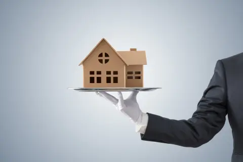 Dłoń w białej rękawiczce podaje model domu na tacy. Czy to oferta z maksymalną prowizją pośrednika nieruchomości?