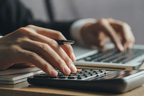 Ręce liczą na kalkulatorze i piszą na laptopie. Kluczowe pytanie: ile trzeba zarabiać żeby dostać kredyt na mieszkanie?
