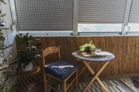 Przytulna loggia z drewnianym krzesłem i stolikiem. Rośliny dodają uroku temu balkonowi.