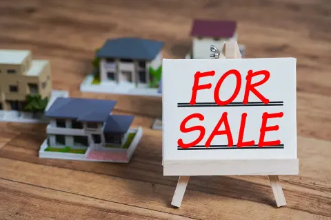 Modele domów na sprzedaż. Czy można sprzedać dom z kredytem? Tabliczka "FOR SALE" na sztaludze.