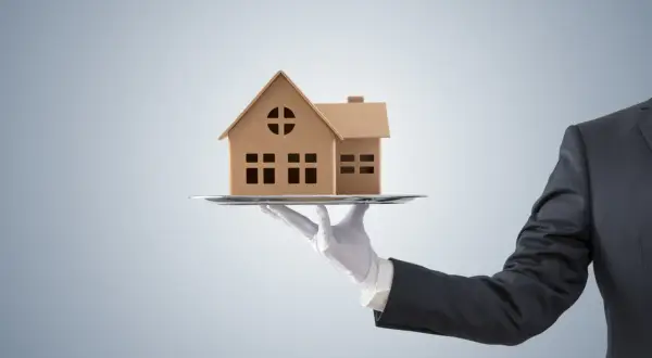 Dłoń w białej rękawiczce podaje model domu na tacy. Czy to oferta z maksymalną prowizją pośrednika nieruchomości?