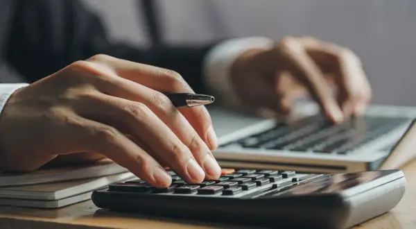 Ręce liczą na kalkulatorze i piszą na laptopie. Kluczowe pytanie: ile trzeba zarabiać żeby dostać kredyt na mieszkanie?