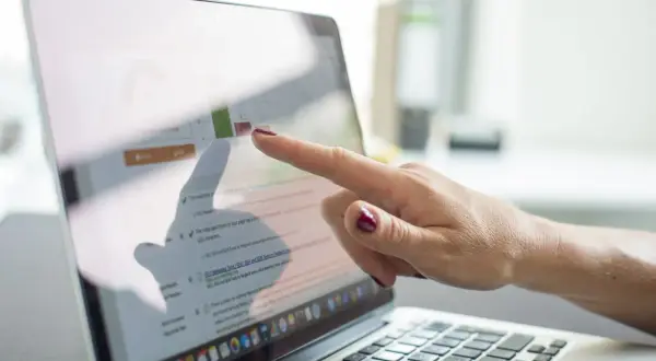 Dłoń wskazuje na ekran laptopa z wykresem i tekstem, prezentując prospekt informacyjny dotyczący optymalizacji SEO.