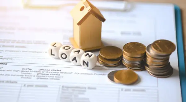Domki, kostki z napisem LOAN, monety i dokumenty. Dylemat: lepiej zmniejszyć ratę czy skrócić okres kredytowania?