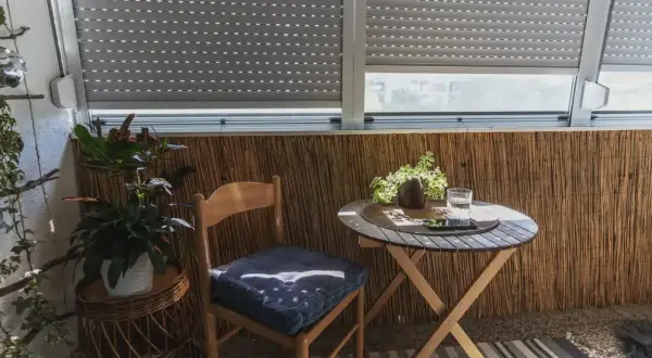 Przytulna loggia z drewnianym krzesłem i stolikiem. Rośliny dodają uroku temu balkonowi.