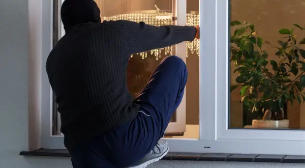 Osoba w kominiarce próbuje dokonać włamania do mieszkania w bloku, wspinając się przez otwarte okno.