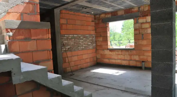 Wnętrze w budowie, widoczna klatka schodowa i ściany z pustaków ceramicznych. Trwa samowolne przekształcenie budynku gospodarczego na mieszkalny.