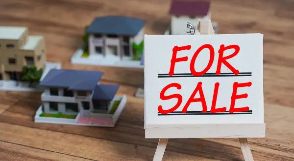 Modele domów na sprzedaż. Czy można sprzedać dom z kredytem? Tabliczka "FOR SALE" na sztaludze.