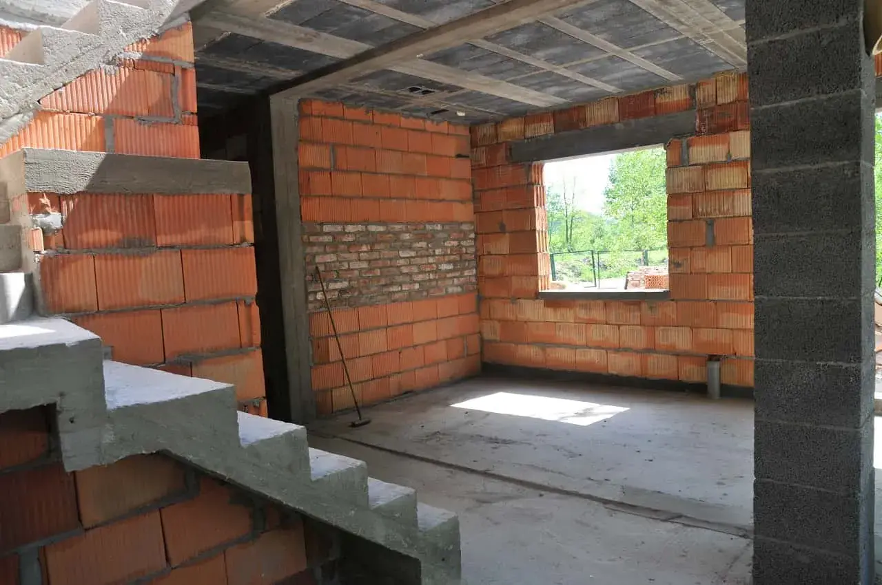 Wnętrze w budowie, widoczna klatka schodowa i ściany z pustaków ceramicznych. Trwa samowolne przekształcenie budynku gospodarczego na mieszkalny.