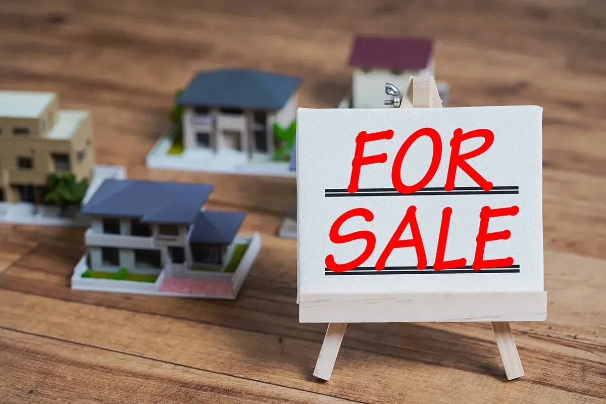 Modele domów na sprzedaż. Czy można sprzedać dom z kredytem? Tabliczka "FOR SALE" na sztaludze.
