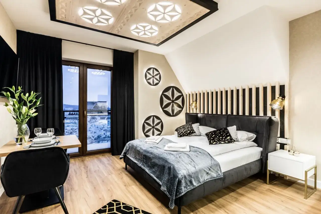 Nowoczesny apartament inwestycyjny z wygodnym łóżkiem, designerskim sufitem i widokiem na zimowy krajobraz.