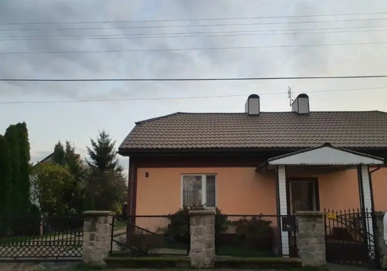 Dom z pomarańczową elewacją i brązowym dachem, ogrodzony płotem. Może czekać go licytacja nieruchomości za mały dług.