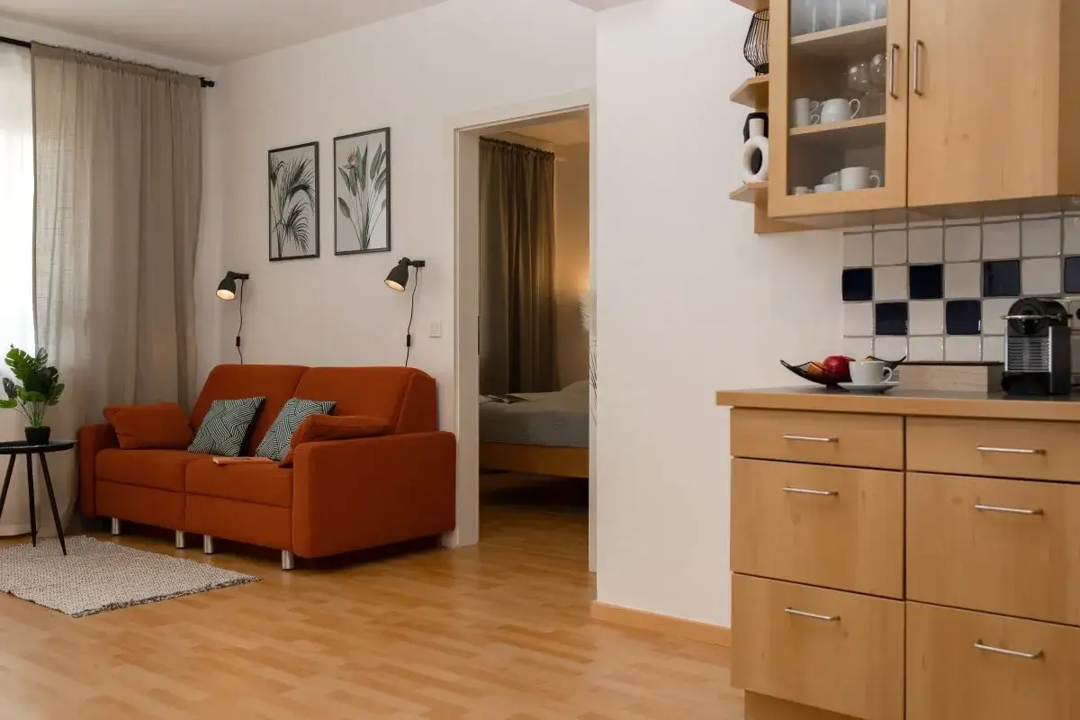 Przytulny salon z pomarańczową kanapą i widokiem na sypialnię. Zwróć uwagę na funkcjonalność i styl, gdy zastanawiasz się, na co zwrócić uwagę przy kupnie mieszkania.