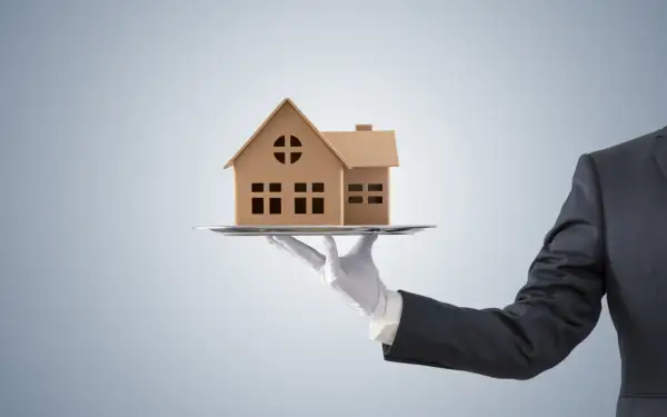 Dłoń w białej rękawiczce podaje model domu na tacy. Czy to oferta z maksymalną prowizją pośrednika nieruchomości?