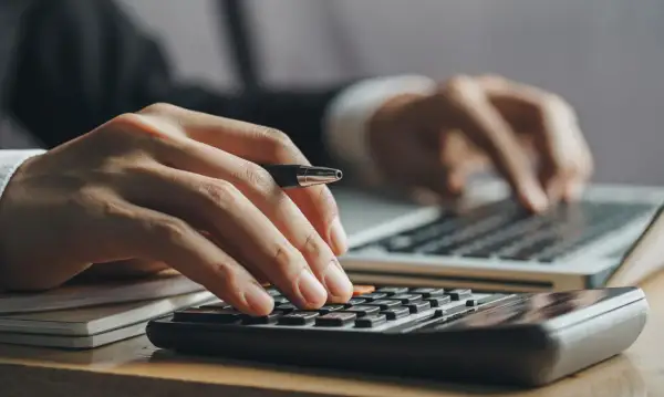 Ręce liczą na kalkulatorze i piszą na laptopie. Kluczowe pytanie: ile trzeba zarabiać żeby dostać kredyt na mieszkanie?