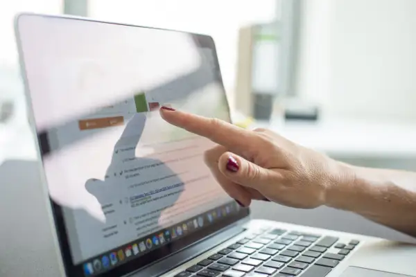 Dłoń wskazuje na ekran laptopa z wykresem i tekstem, prezentując prospekt informacyjny dotyczący optymalizacji SEO.