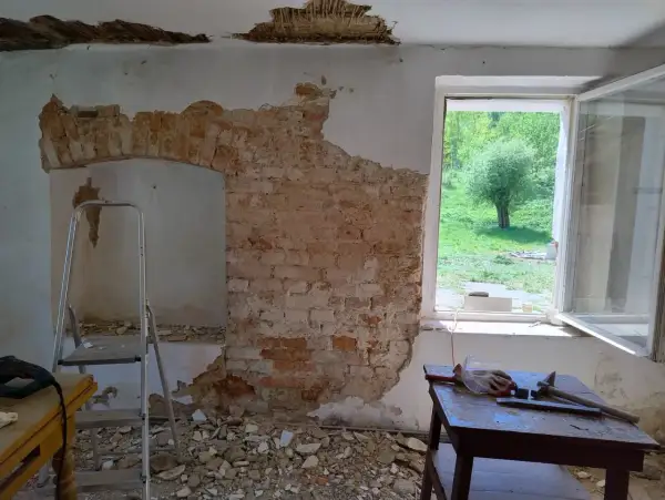 Ekspertyza budowlana starego domu: odsłonięta cegła, drabina i narzędzia wskazują na remont.