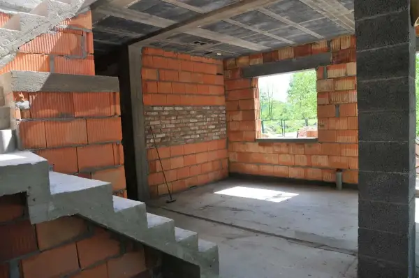 Wnętrze w budowie, widoczna klatka schodowa i ściany z pustaków ceramicznych. Trwa samowolne przekształcenie budynku gospodarczego na mieszkalny.